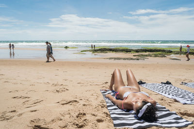 People lying on beach against sky