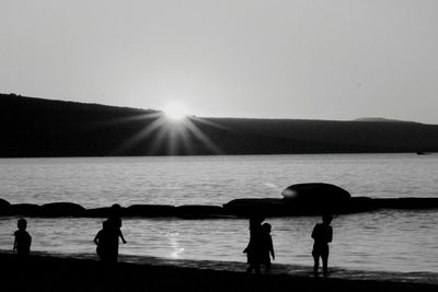 Silhouette people at beach against clear sky during sunset