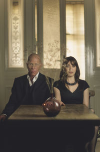 Portrait of man and woman sitting by flower vase on table at home