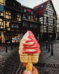 Cropped hand holding ice cream cone against built structure