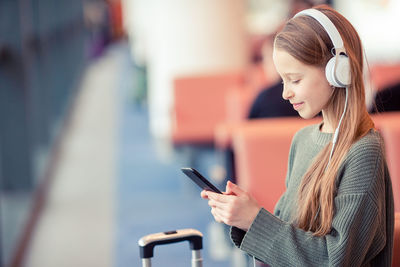 Side view of girl using mobile phone while standing at airport