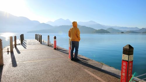 Rear view of man standing on pier in lake