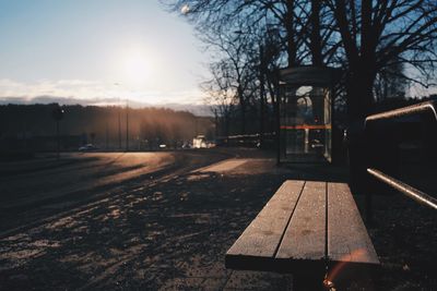 Empty bench by street against sky during sunset