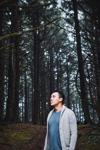 Thoughtful young man looking up while standing in forest