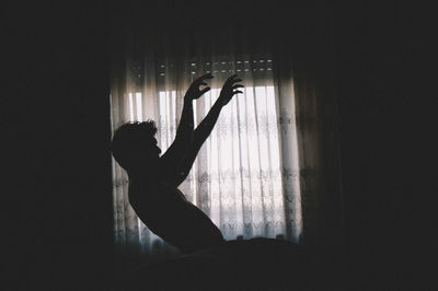 Silhouette man falling on bed against curtain in darkroom