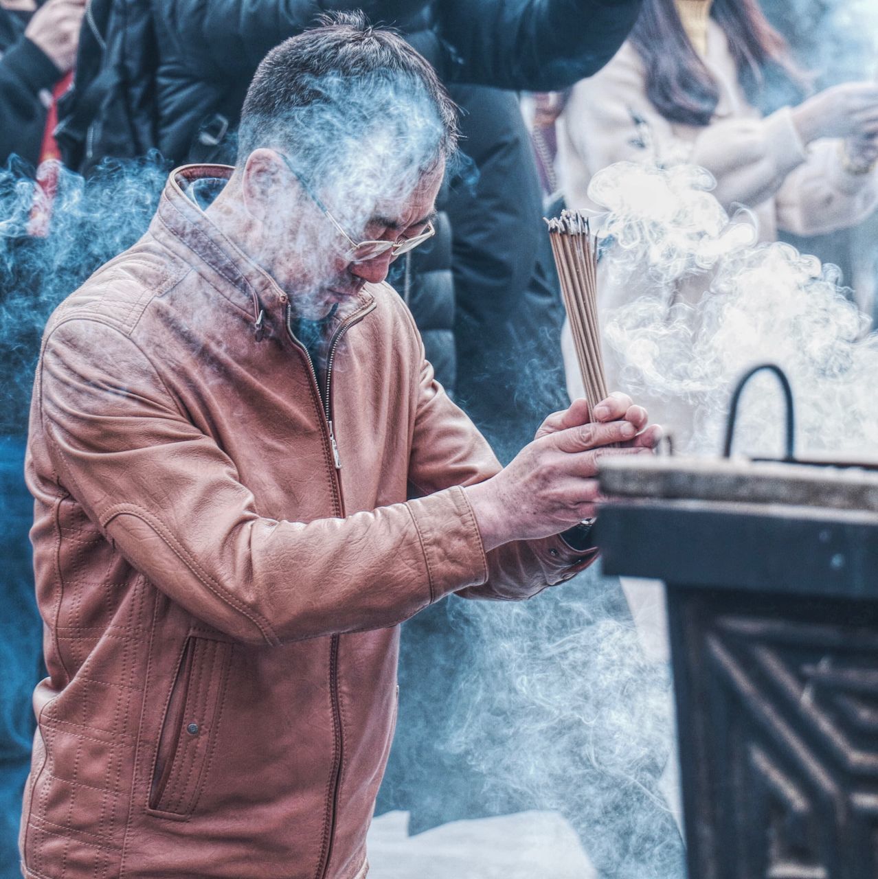 men, smoke - physical structure, real people, people, males, adult, holding, belief, incidental people, working, focus on foreground, spirituality, day, three quarter length, religion, senior adult, lifestyles, place of worship, standing