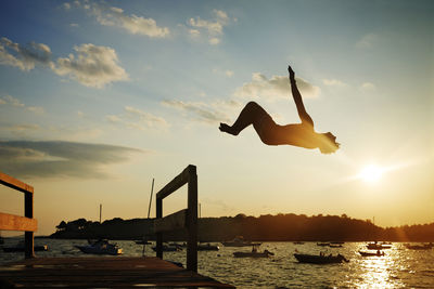 Silhouette man backflipping into sea against sky during sunset