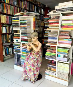 Full length of woman standing by books in shelf