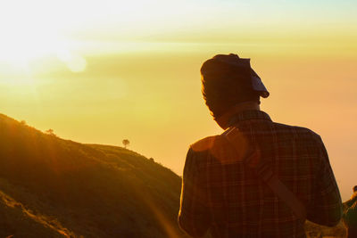 Rear view of man standing on mountain against sky during sunset
