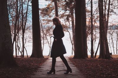 Full length of woman standing amidst trees in forest