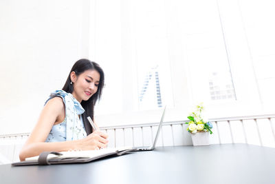 Young woman using mobile phone while sitting on table