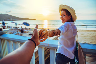 Midsection of man standing by railing against sea during sunset