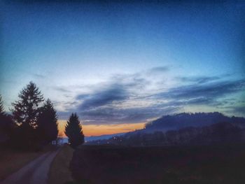 Silhouette trees by road against sky at sunset