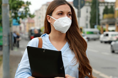 Woman in mask looking away while standing in city