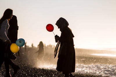 People with balloons on field against sky