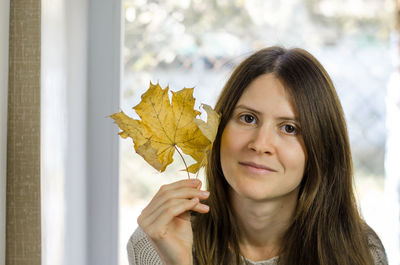 Portrait of young woman holding maple leaf