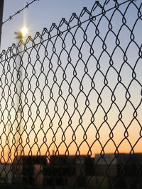 Close-up of chainlink fence against sky during sunset