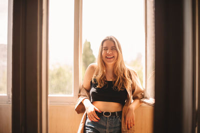 Happy young woman laughing while standing in balcony during summer