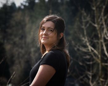 Side view portrait of woman standing against trees