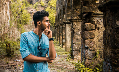 Thoughtful young man looking away while standing at old ruins