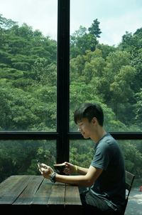 Side view of man using mobile phone against window