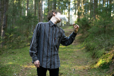 Full length of man standing in forest taking off his mask