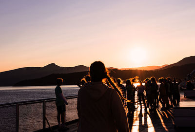 People looking at mountains against sky during sunset