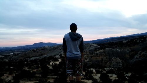 Rear view of man standing on mountain against sky