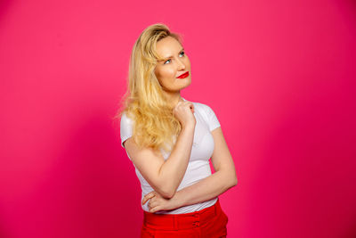 Portrait of woman standing against pink background