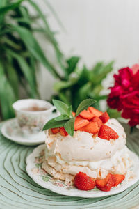 Dessert cake with cream and strawberries on the background of home plants on a small table