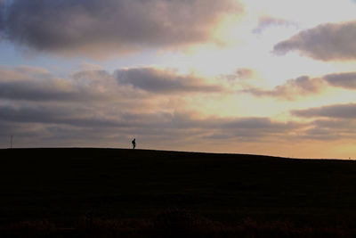 Silhouette of man on field against sky at sunset