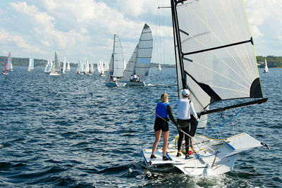 Rear view of men sailing on sea against sky