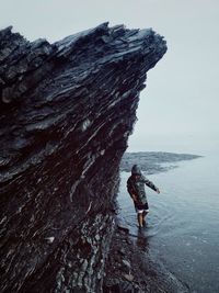 Boy standing on rock by sea against sky