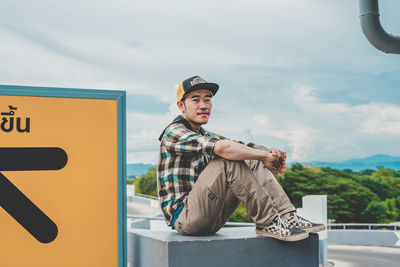 Full length of young man sitting against sky