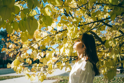 Side view of young woman with eyes closed standing by tree in park during sunny day