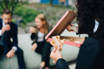 Cropped image of businesswoman holding pizza against colleagues