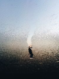 Close-up of wet glass window against sky