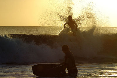 Friends on sea shore against sky during sunset