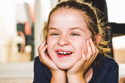 Smiling girl with hands on chin looking away while sitting at home