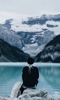 Rear view of woman sitting by lake against mountains