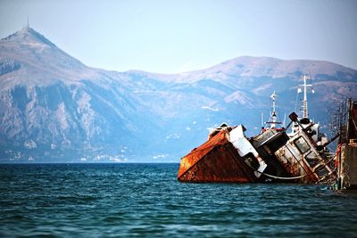 Rusty ship in sea by mountains