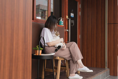 Asian woman wearing protective mask sit and play with her cat at outdoor coffee shop