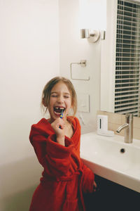 Cute little girl in red robe brushing her teeth in bathroom at night 