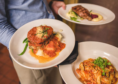 Midsection of waiter holding food in plates at restaurant