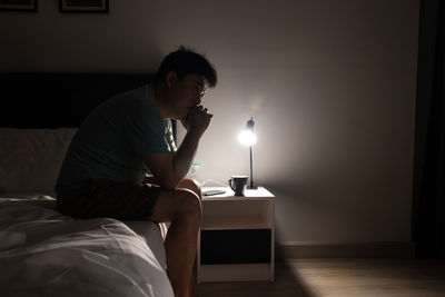 Side view of man sitting on bed at home