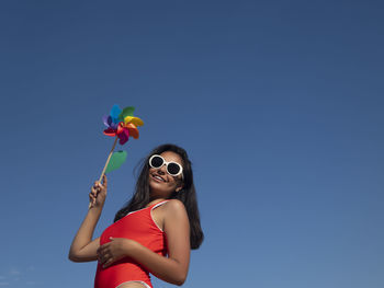 Low angle view of woman wearing sunglasses against clear blue sky