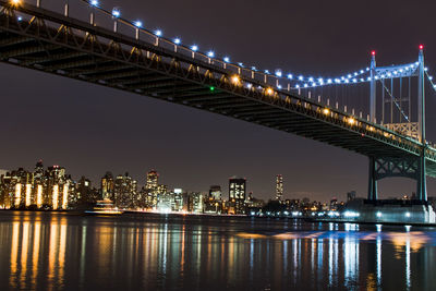 Illuminated cityscape by river against sky at night