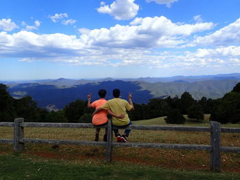 Rear view of couple gesturing peace sign while looking at mountains against sky