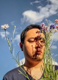 Young asian man with cornflowers casting shadow patterns onto his face against cloudy blue sky