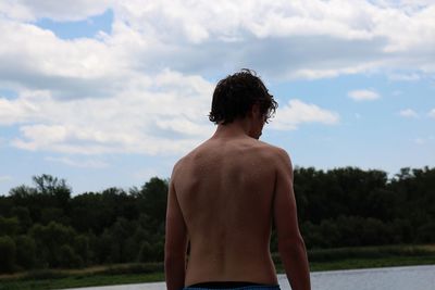 Rear view of shirtless boy standing against sky